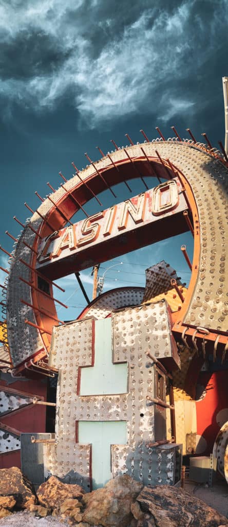 A collection of neon signs in salvage condition, including an H and a horseshoe. The sky behind is blue with white clouds.