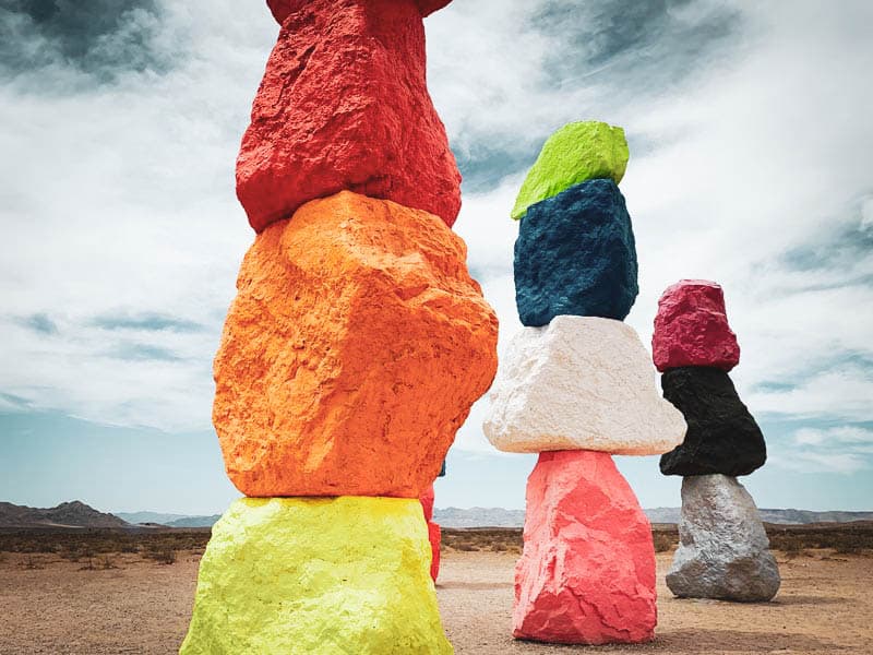 An art installation in the desert. Large, neon painted boulders are stacked on top of each other.