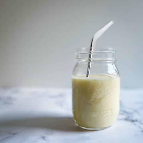 A banana mango gluten free AIP smoothie in a glass jar with metal straw