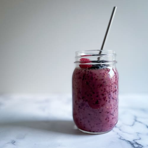 A purple berry AIP Dairy Free Gluten Free smoothie in a jar with a metal straw