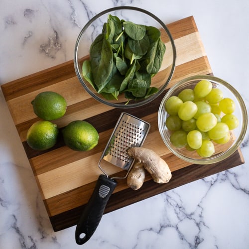 Grapes, limes, spinach, and ginger on a cutting board