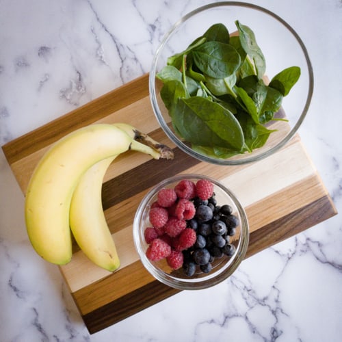 Banana, blueberries, raspberries, and spinach on a cutting board