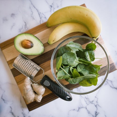 Banana, avocado, ginger, and spinach on a wooden cutting board