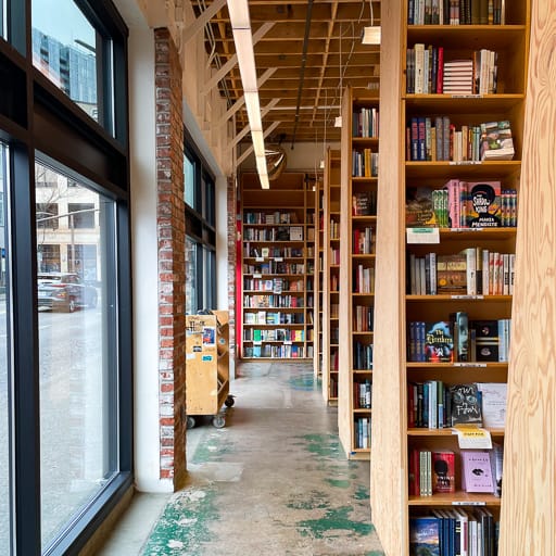 An aisle in a bookstore with windows on one side and bookshelves on the other side