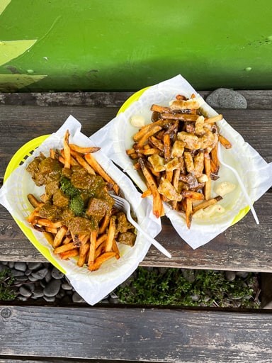 Two baskets of gluten free fries with toppings sitting on a wooden table from Potato Champion in Portland