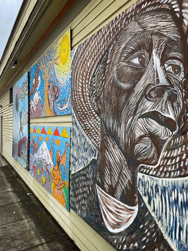 A mural of people and camels on the side of a building in blues, browns, and oranges